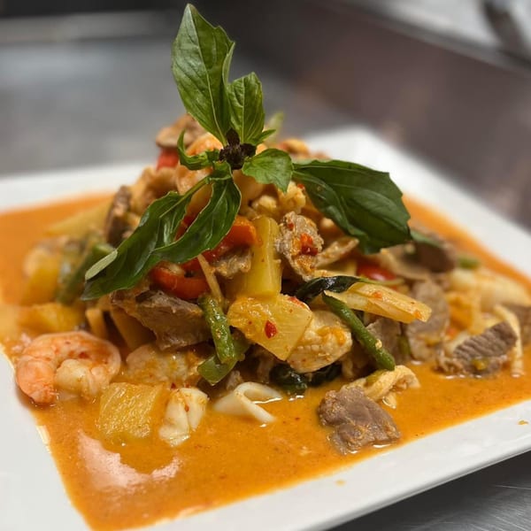 A vibrant Thai red curry with shrimp, beef, chicken, and vegetables, garnished with fresh basil.