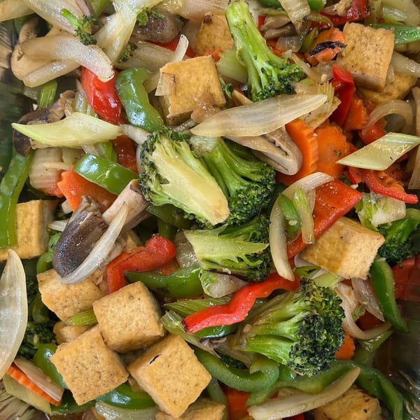 Close-up of a vibrant Thai stir-fry with tofu, broccoli, bell peppers, onions, and carrots.