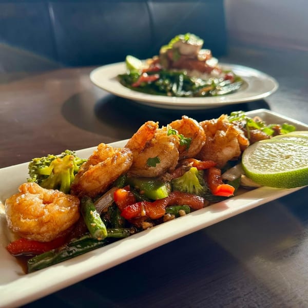 Crispy fried shrimp with stir-fried vegetables and lime wedges on a white rectangular plate.